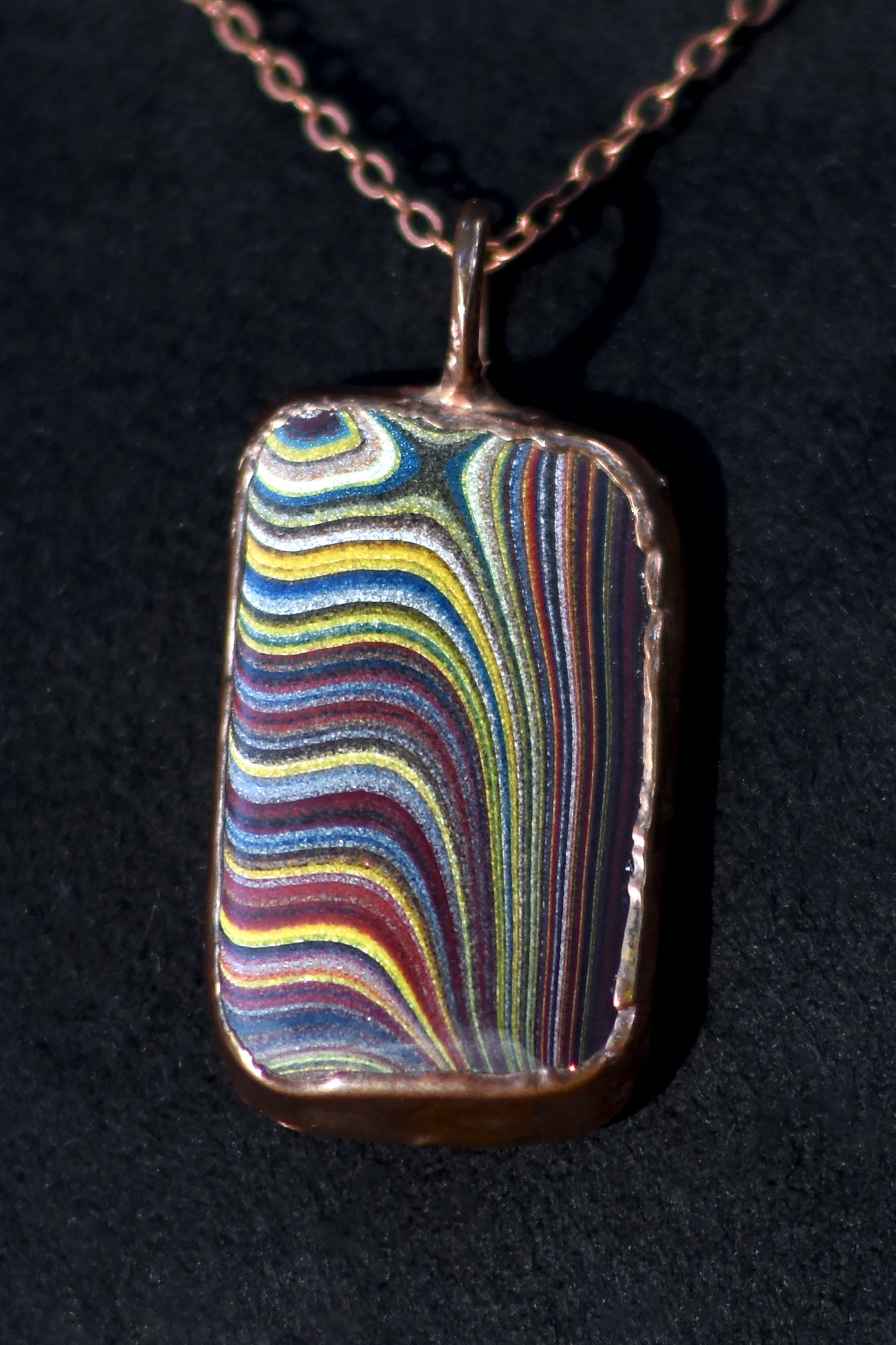 Multicolored Fordite pendant on a chain against a black background